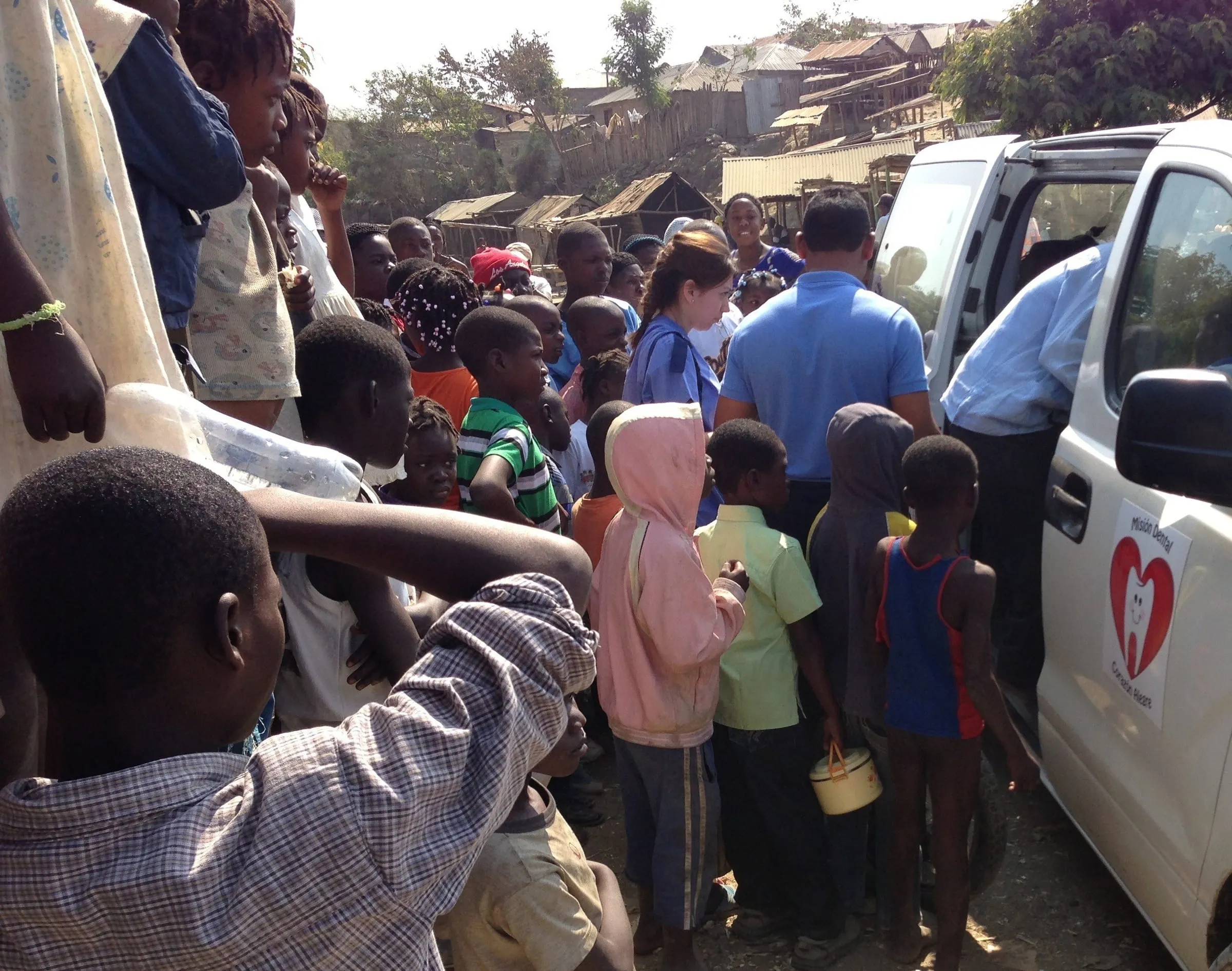 Children crowd excitedly around the Cheerful Heart Mission van as it arrives