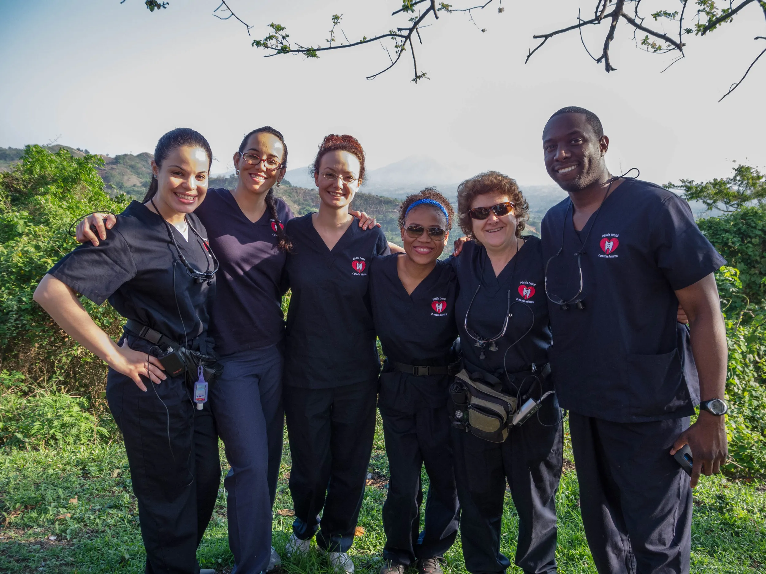 Six smiling Cheerful Heart Mission volunteers in scrubs pose together outdoors