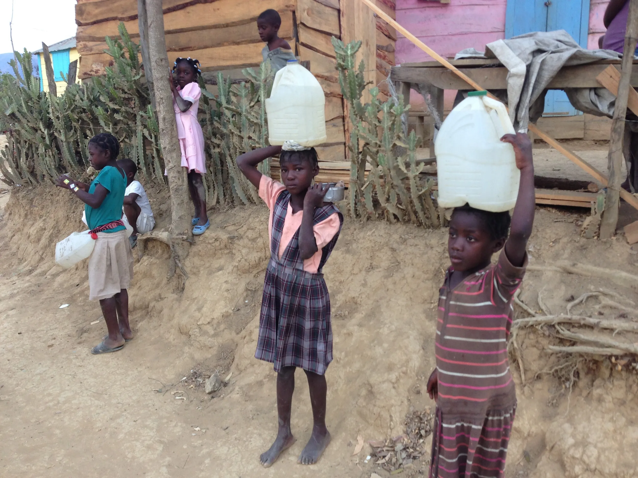 Young girls carry heavy water jugs on their heads along a dirt path