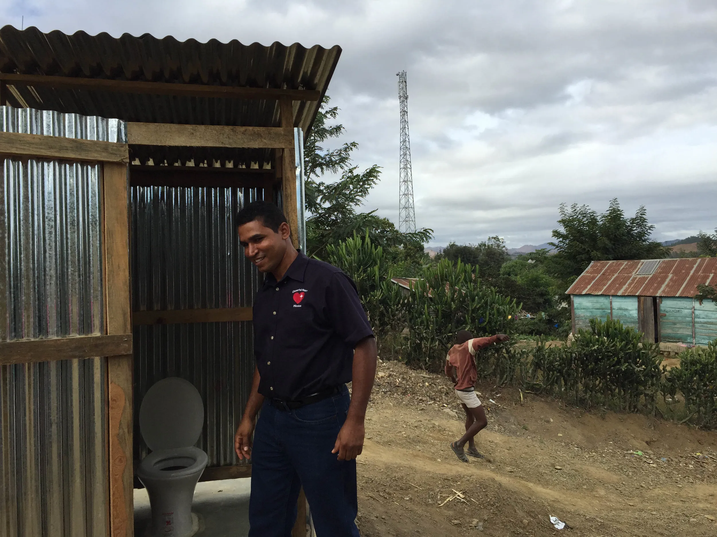 A Cheerful Heart Mission staff member stands beside a newly constructed latrine in Haiti