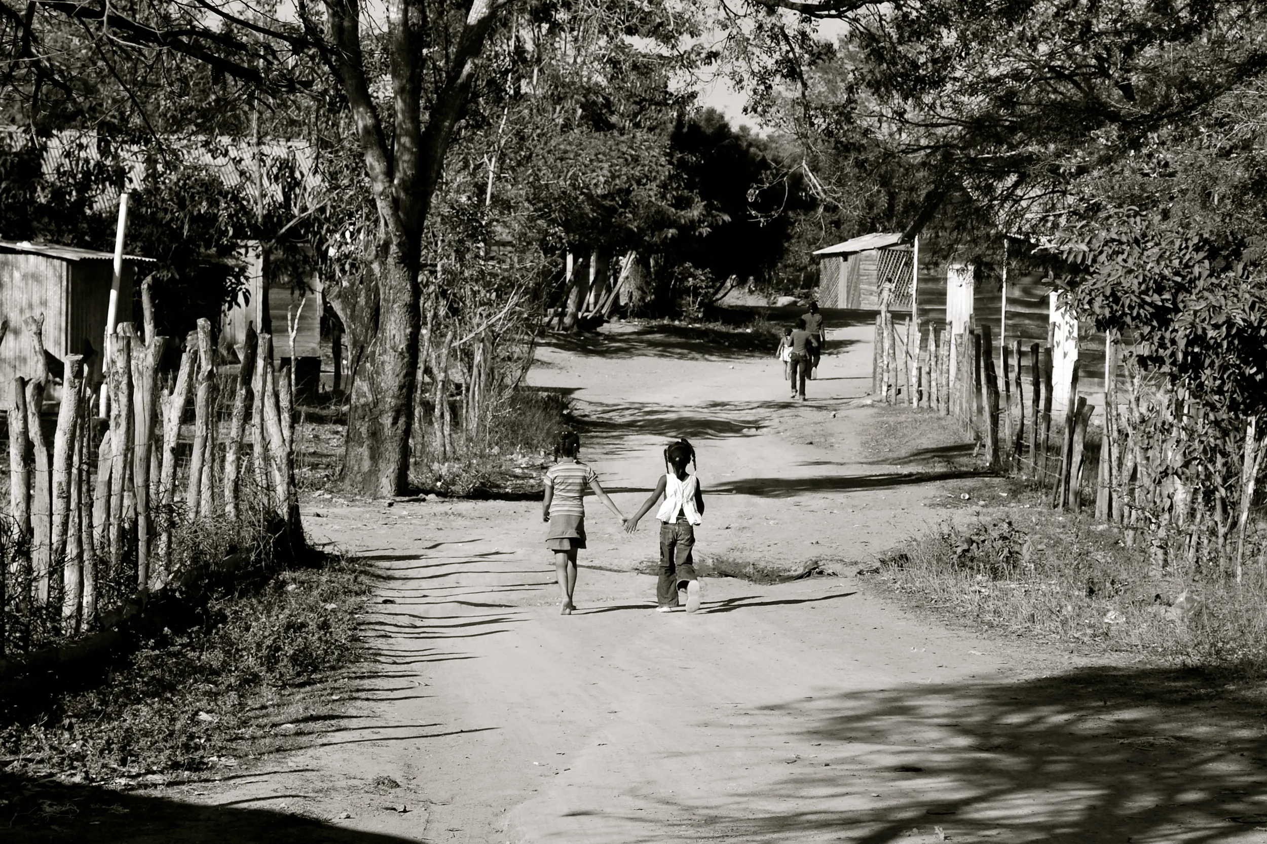 Black-and-white photo of two children walking down a rural tree-lined road