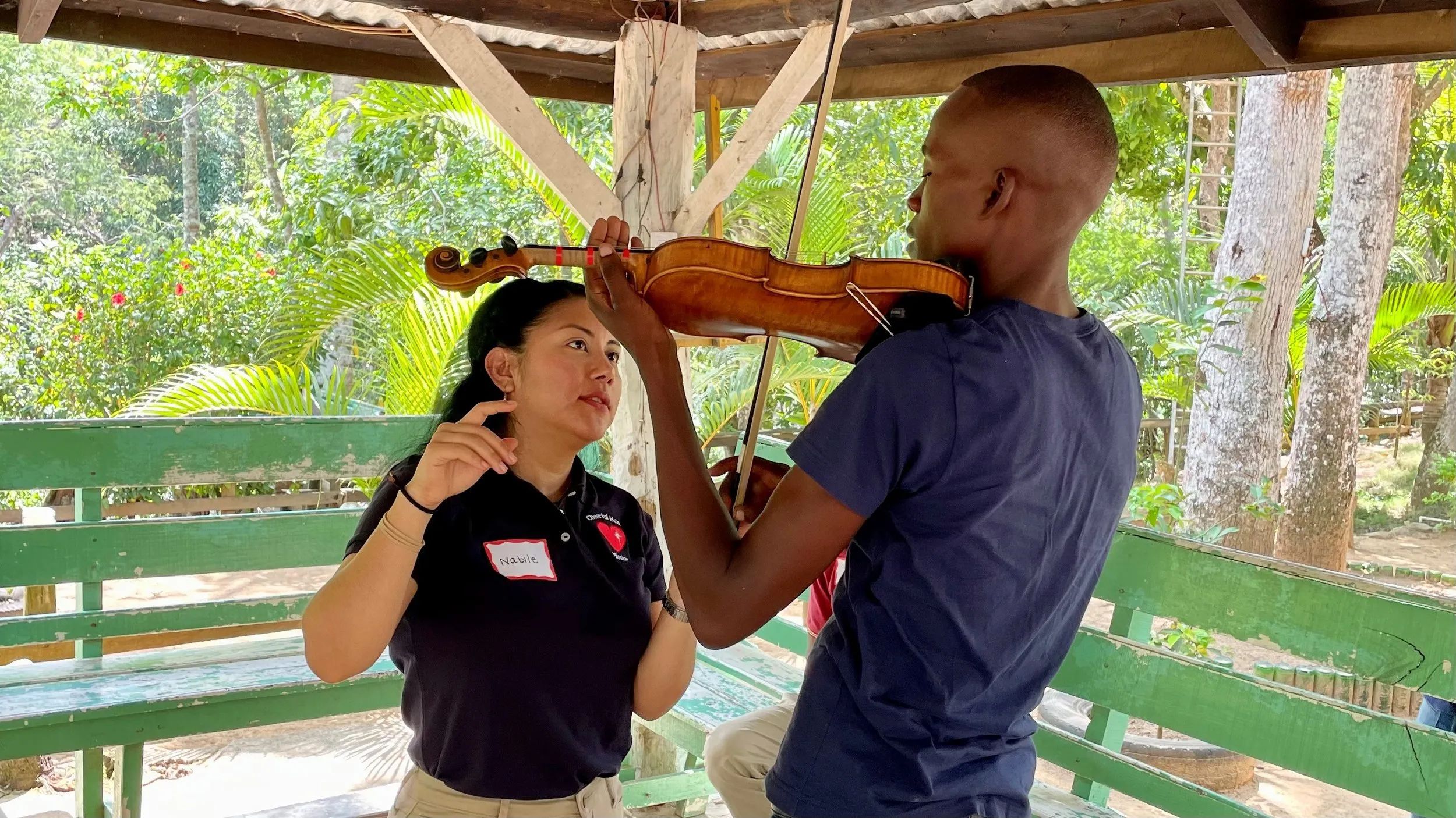 A music instructor gives a student a violin lesson in an outdoor gazebo