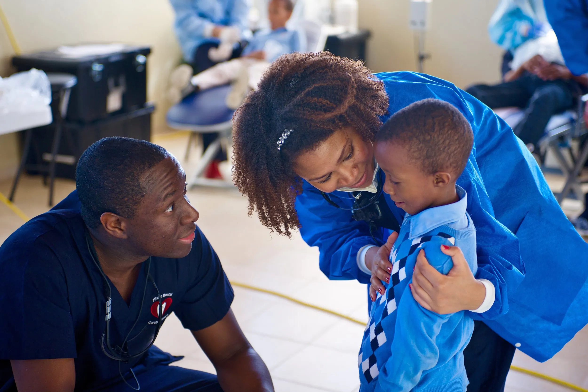 Two Cheerful Heart Mission volunteers smile and comfort a small boy